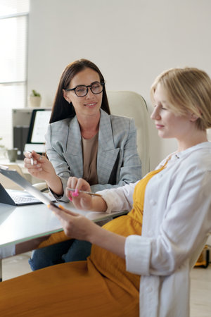 Vertical image of young pregnant woman having consultation with manager in officeの写真素材