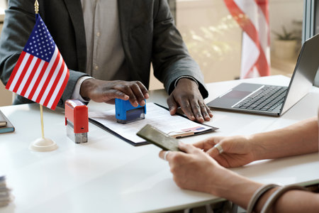 Close-up of African American manager putting seals on visa document during meeting with clientの写真素材