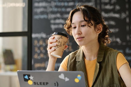 Student sitting at desk in the classroom and drinking coffee during online lessonの写真素材