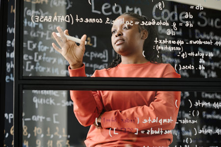 African American teacher standing near the glass board and explaining computer codes at lessonの写真素材