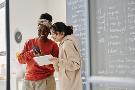 African American teacher showing online presentation on smartphone to student at IT lessonの写真素材
