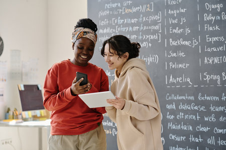 IT teacher discussing computer program on smartphone together with student at IT lessonの写真素材
