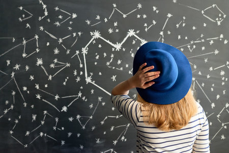 Rear view of female astrologer looking at blackboard with pictured constellation of stars in shape of heartの写真素材