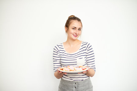Pretty young woman holding plate with homemade cookies and looking at cameraの写真素材