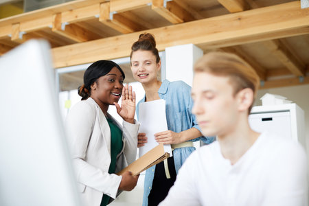 Positive multi-ethnic employees gossiping about male colleague using computer in officeの写真素材