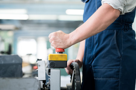 Close-up of unrecognizable factory worker in overall operating industrial machine with remote control, he pushing ed button while launching conveyorの写真素材