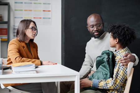 Young teacher talking to father of boy about his behavior while they sitting in classroom after lessonsの写真素材