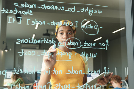 African American student using tablet pc and writing formulas on glass wall during lessonの写真素材
