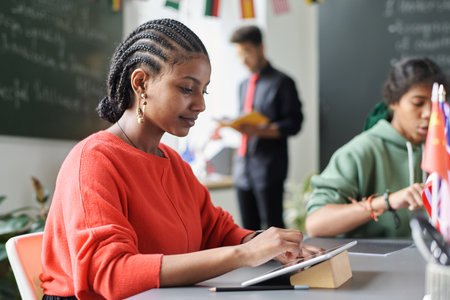African American student using digital tablet while sitting at table with her classmates during lessonの写真素材