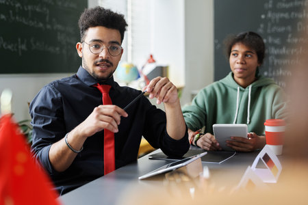 Young teacher sitting at desk and teaching students in classの写真素材