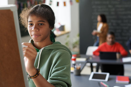 African American schoolgirl writing on blackboard in the classroom during lessonの写真素材