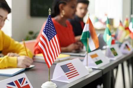 Close-up of flags of different countries standing on table with multiracial students studying in backgroundの写真素材