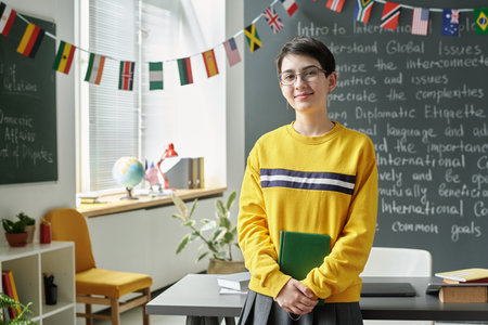Portrait of schoolgirl with book looking at camera while standing in the classroomの写真素材