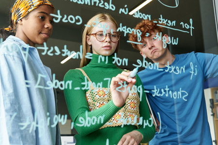 Group of students writing codes on glass wall and discussing it in team in the classroomの写真素材