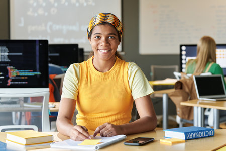 Portrait of African American student smiling at camera while sitting at desk and studying IT at schoolの写真素材