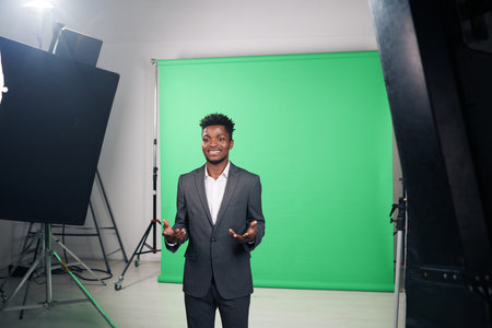African American correspondent in suit telling news for TV program while standing in professional studio with equipmentの写真素材