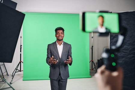African American man in suit recording video content on smartphone in professional studioの写真素材
