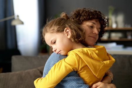 Young mom embracing and calming her child while he in bad mood or upset feelingsの写真素材
