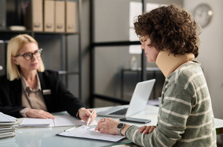 Side view portrait of young woman with neck injury filling documents at insurance agency office, copy spaceの写真素材
