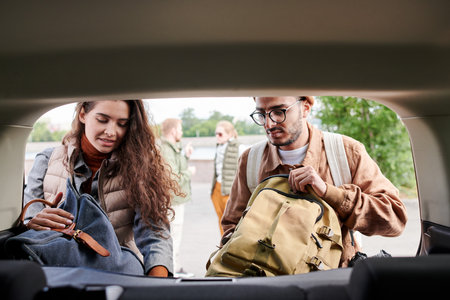 Young multi-ethnic friends loading bags into car trunk while preparing for travelの写真素材