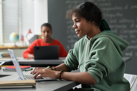 African American schoolgirl sitting at table in the classroom and using laptop in her studyの写真素材
