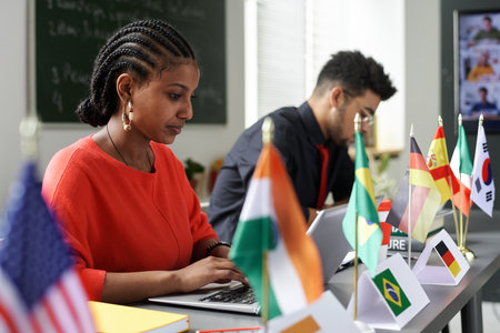 Group of international students sitting at table with flags and using gadgets at lesson in the classroomの写真素材