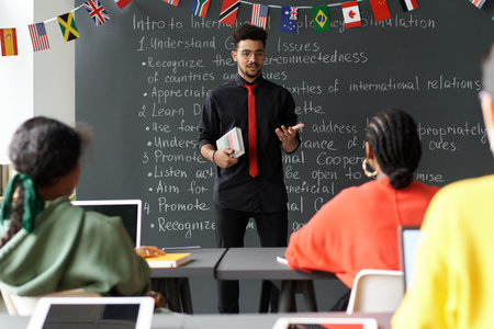 Young teacher standing near the blackboard and having lesson with students in the classroomの写真素材
