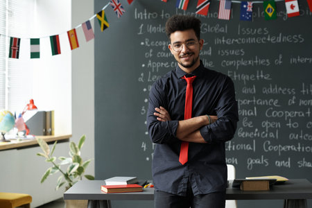 Portrait of Arabic student standing with his arms crossed against the blackboard and smiling at cameraの写真素材