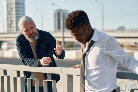 Mature man trying to help the young guy with conversation while they standing on the bridge in the cityの写真素材
