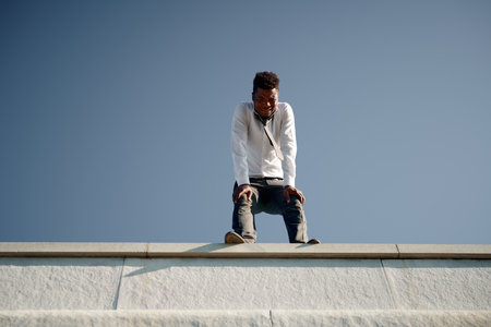 Low angle view of depressed man standing on the edge of the roof and cryingの写真素材