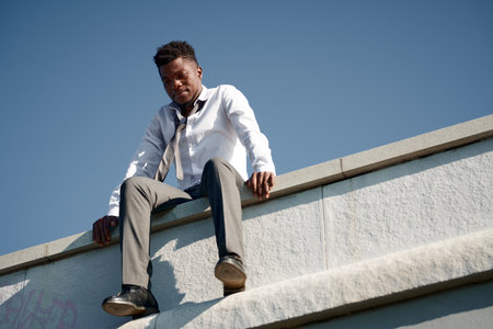 Low angle view of upset guy sitting on the edge of the roof and trying to commit suicideの写真素材
