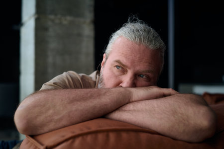 Man in depression sitting on sofa at home and thinking about his problemsの写真素材