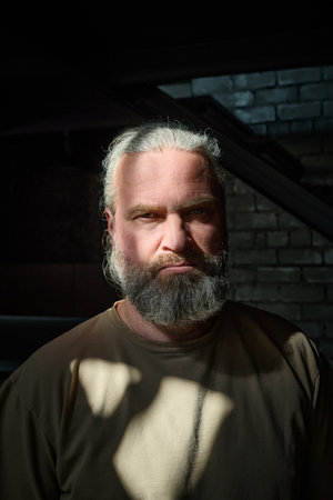 Vertical portrait of mature man looking at camera with serious sight while staying alone at homeの写真素材