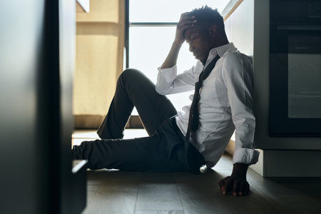 African American man suffering from depression sitting on the floor in the kitchenの写真素材