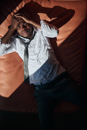 Top view of African American man having a headache he lyin gon sofa and holding his headの写真素材
