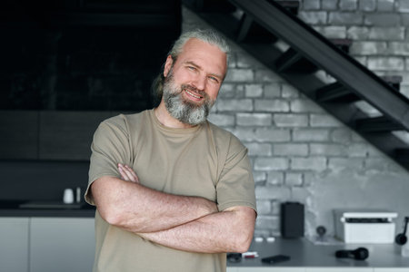 Portrait of mature man smiling at camera while standing with his arms crossed in modern kitchen