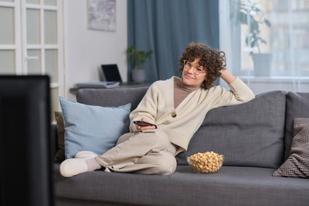 Young woman watching TV in the living room while sitting on sofa with popcornの写真素材