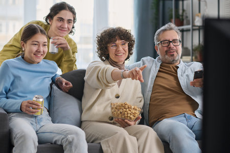 Happy family of four eating popcorn and enjoying watching movie together at homeの写真素材