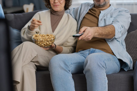 Couple sitting on sofa, eating popcorn and watching TV together at home
