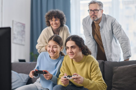 Children using joysticks to play video game together with their parents at homeの写真素材