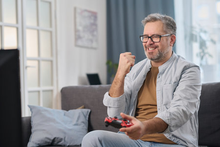 Mature man using joysticks to play video game while sitting on sofa in the living roomの写真素材