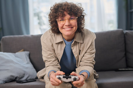 Portrait of happy woman pushing buttons on joystick to play video game on sofa in the roomの写真素材
