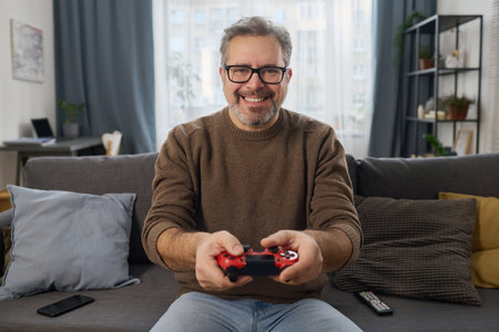 Portrait of happy man pushing buttons on joystick to play video game on sofa in the roomの写真素材