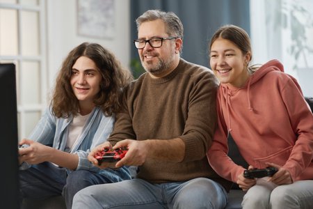 Happy dad playing video game together with his children while they sitting on sofa in the living roomの写真素材