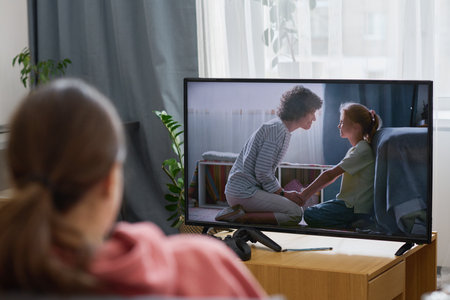 Rear view of girl watching movie while sitting in front of screen in the living roomの写真素材
