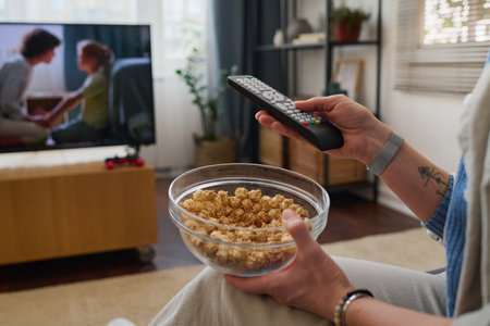 Close-up of woman using remote control while watching movie with popcorn in the roomの写真素材