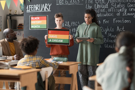 School children standing near the blackboard and giving presentation for classmates and teacher in the classroom during a lessonの写真素材