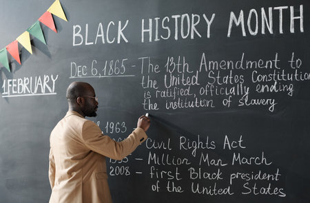 African American teacher writing information about Black History Month on blackboard during a lessonの写真素材