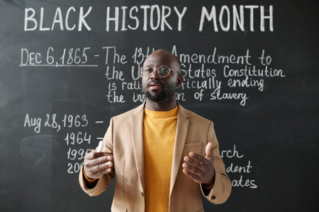 African American teacher standing against the blackboard and talking about the history to studentsの写真素材
