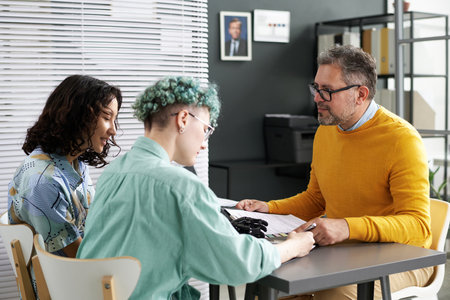 Young women signing documents while sitting in office with consultantの写真素材